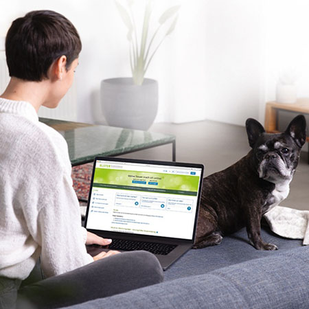 Eine Frau sitzt mit ihrem Hund auf dem Sofa und ruft auf ihrem Laptop MeinELSTER auf.